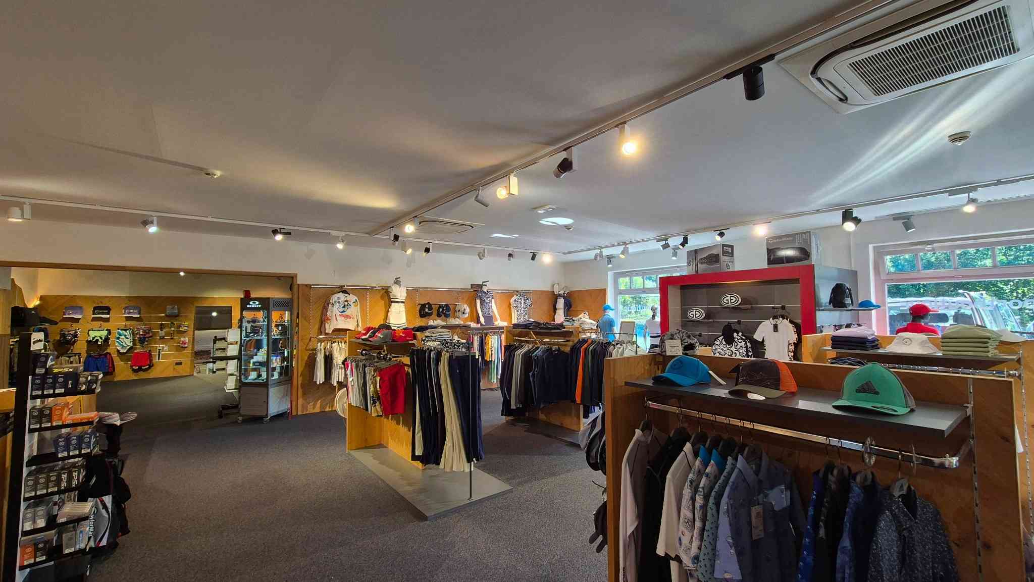 Innenansicht des Proshops Eichenheim mit Sportbekleidung, Caps und Golfzubehör auf Kleiderständern und Regalen