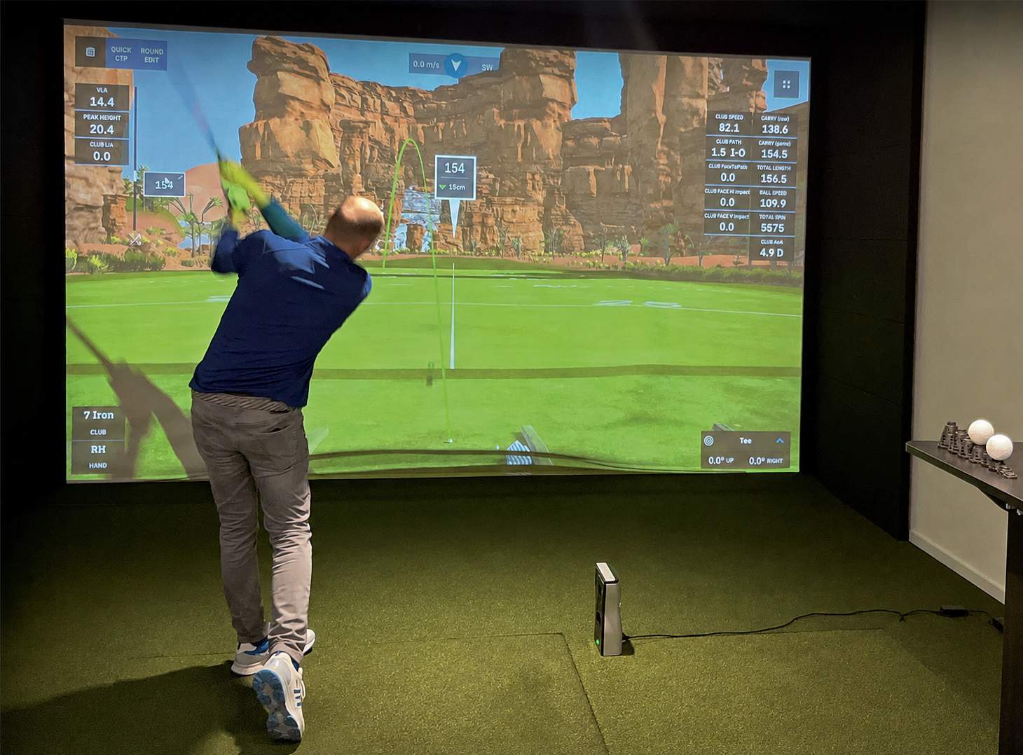 Golfer schlägt in einem Indoor-Golfsimulator, während mehrere Personen das Fitting beobachten