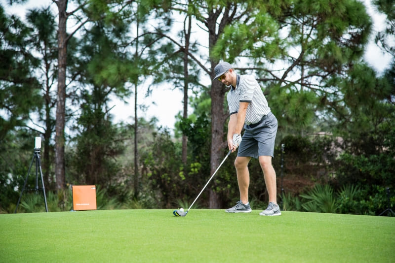 Golfspieler beim Abschlag mit TrackMan Launch Monitor für die Analyse von Schwung, Ballgeschwindigkeit und Flugbahn.